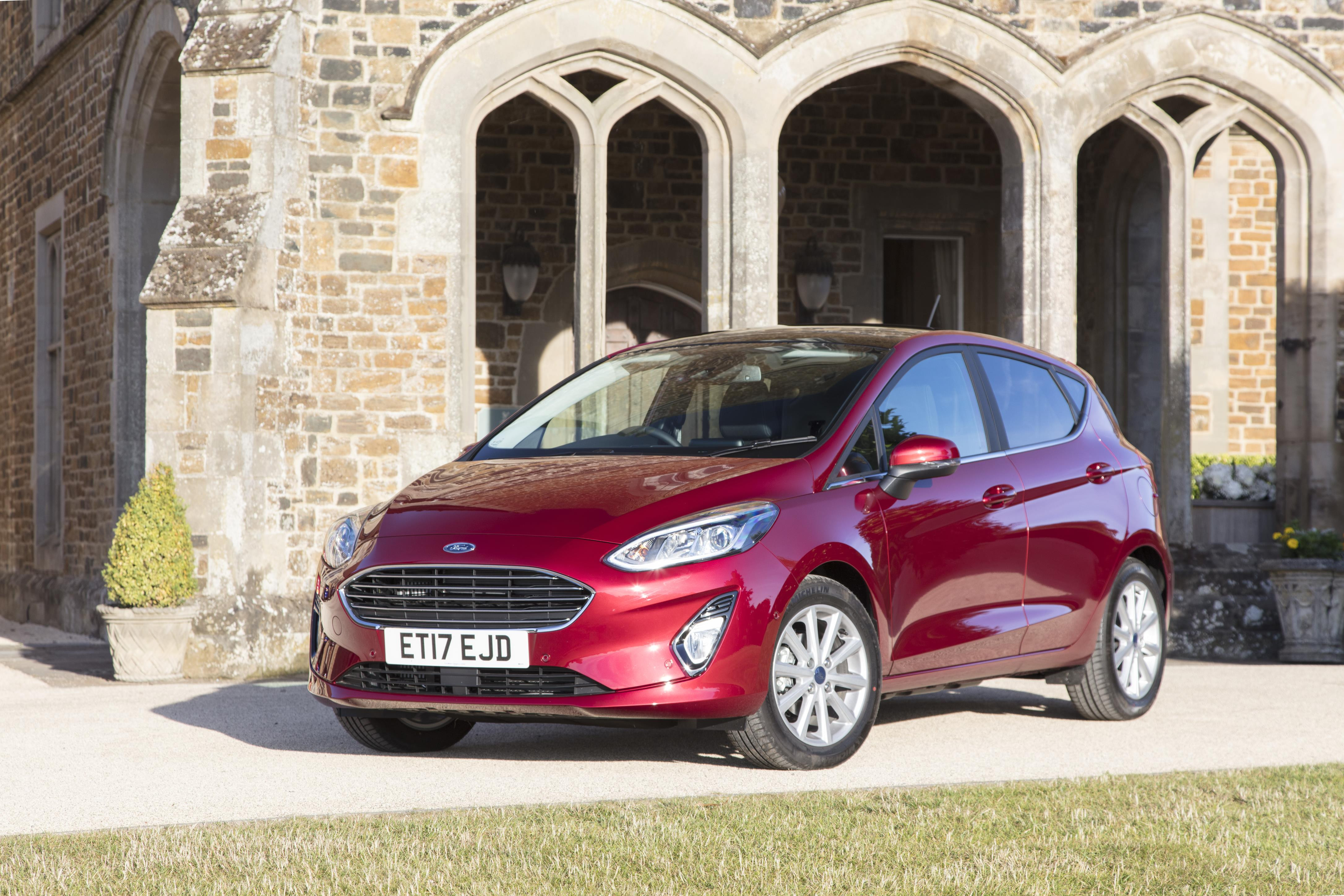 Dark red Ford Fiesta parked facing three-quarters left in front of gothic archways.